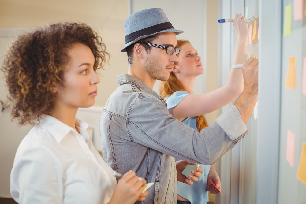 Business people writing on adhesive notes on glass wall during meeting in office